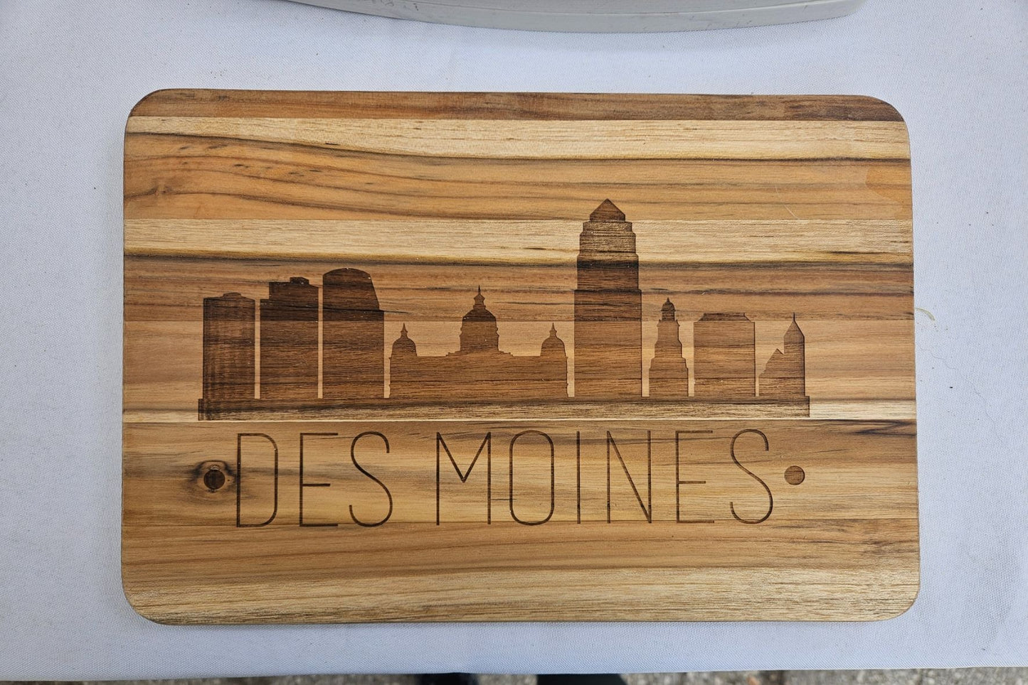 Wooden cutting board with engraved 'Des Moines' and skyline design on a white surface.