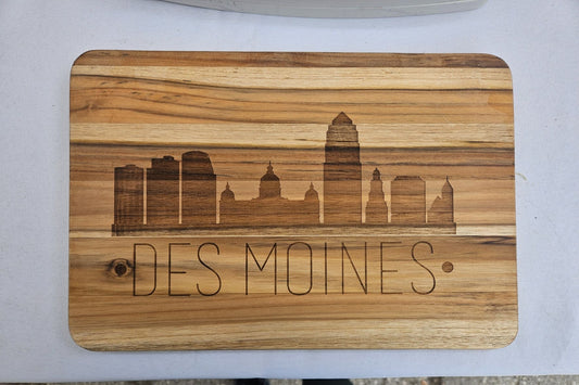 Wooden cutting board with engraved 'Des Moines' and skyline design on a white surface.