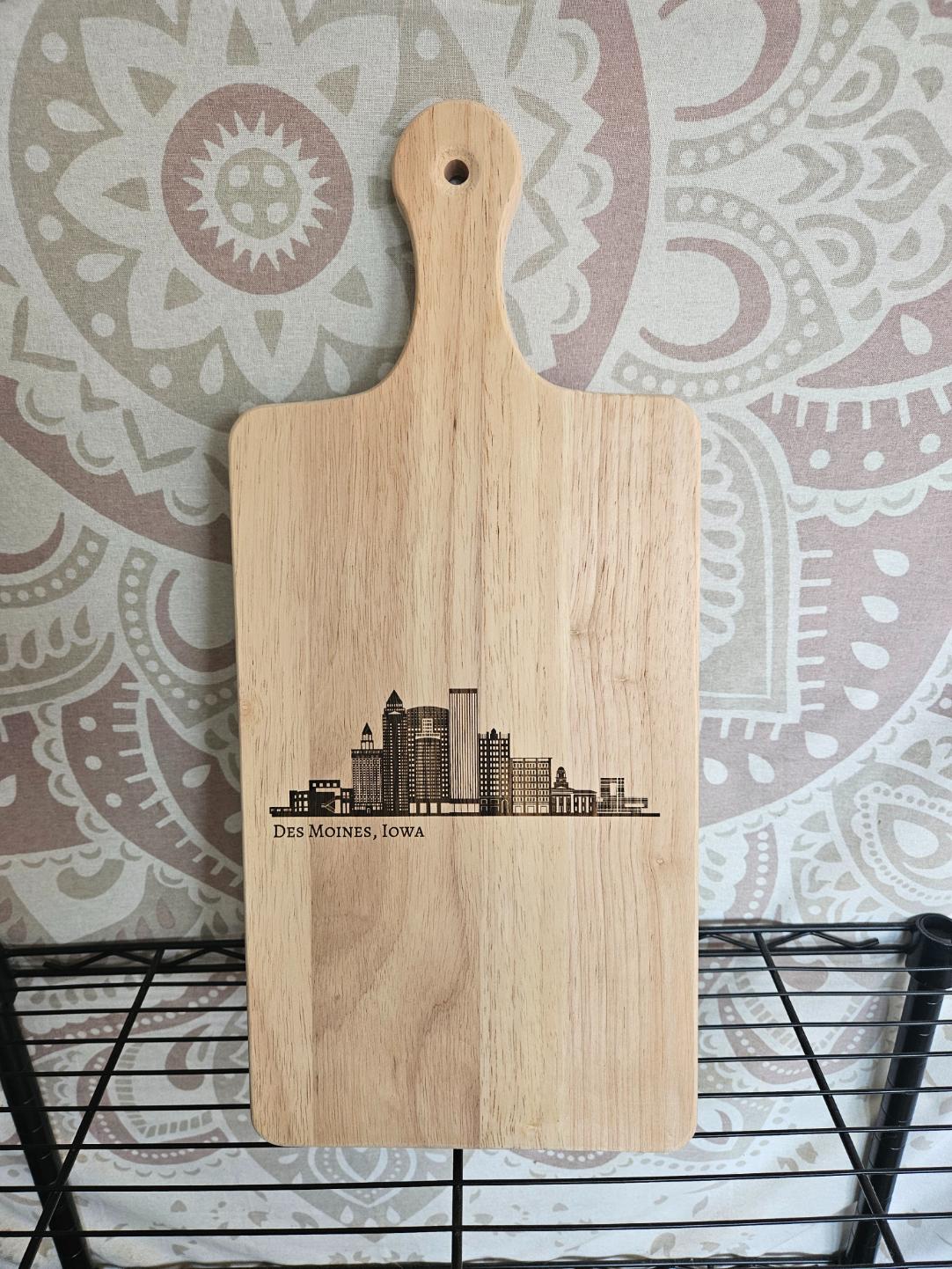 Wooden cutting board with engraved skyline design on a patterned wall background