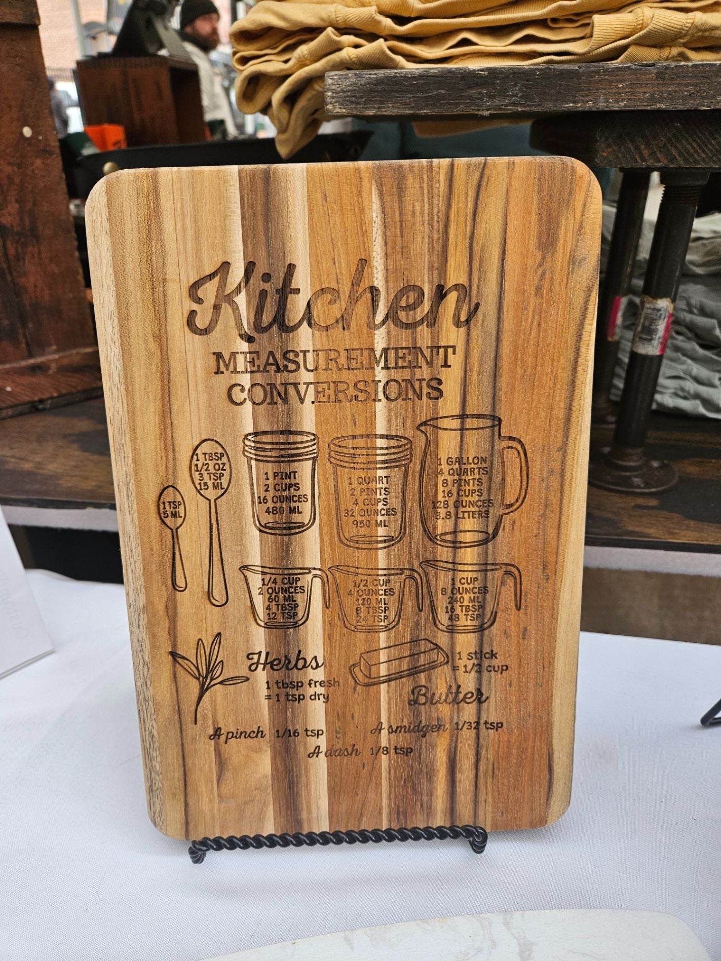 Wooden cutting board with kitchen measurement conversions engraved on it, placed on a white surface.