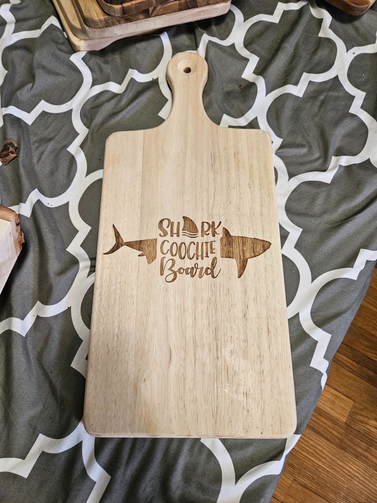 Wooden cutting board with 'Shark Coochie Board' engraving on a patterned surface