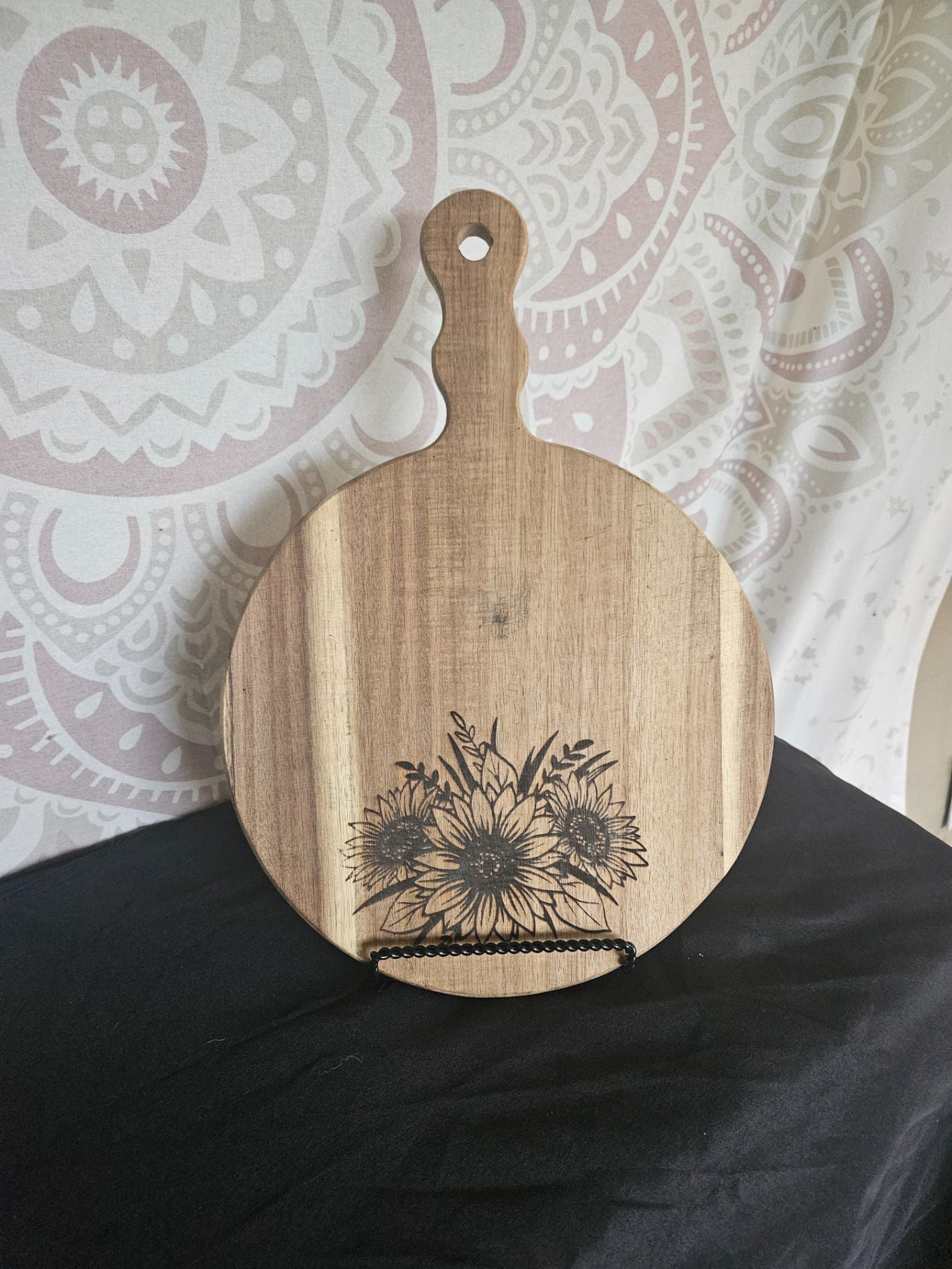Wooden cutting board with floral design on a black surface and patterned background