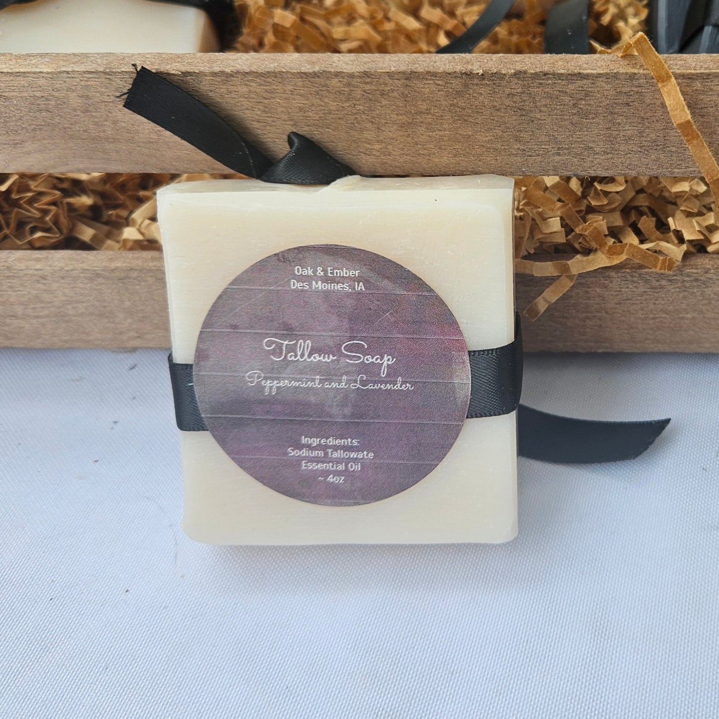 Bar soaps with black ribbons and labels in a wooden crate on a white surface.