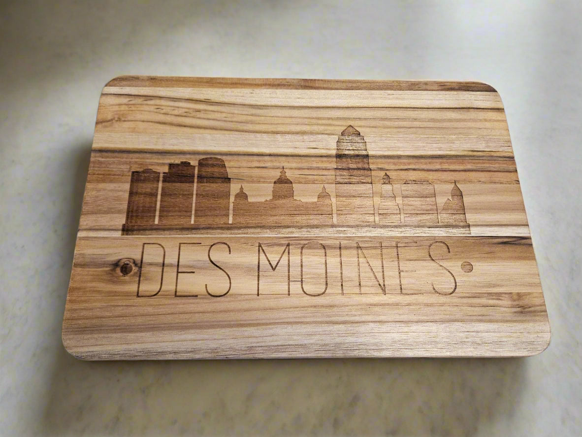 Wooden cutting board with engraved 'Des Moines' and cityscape on a patterned fabric background