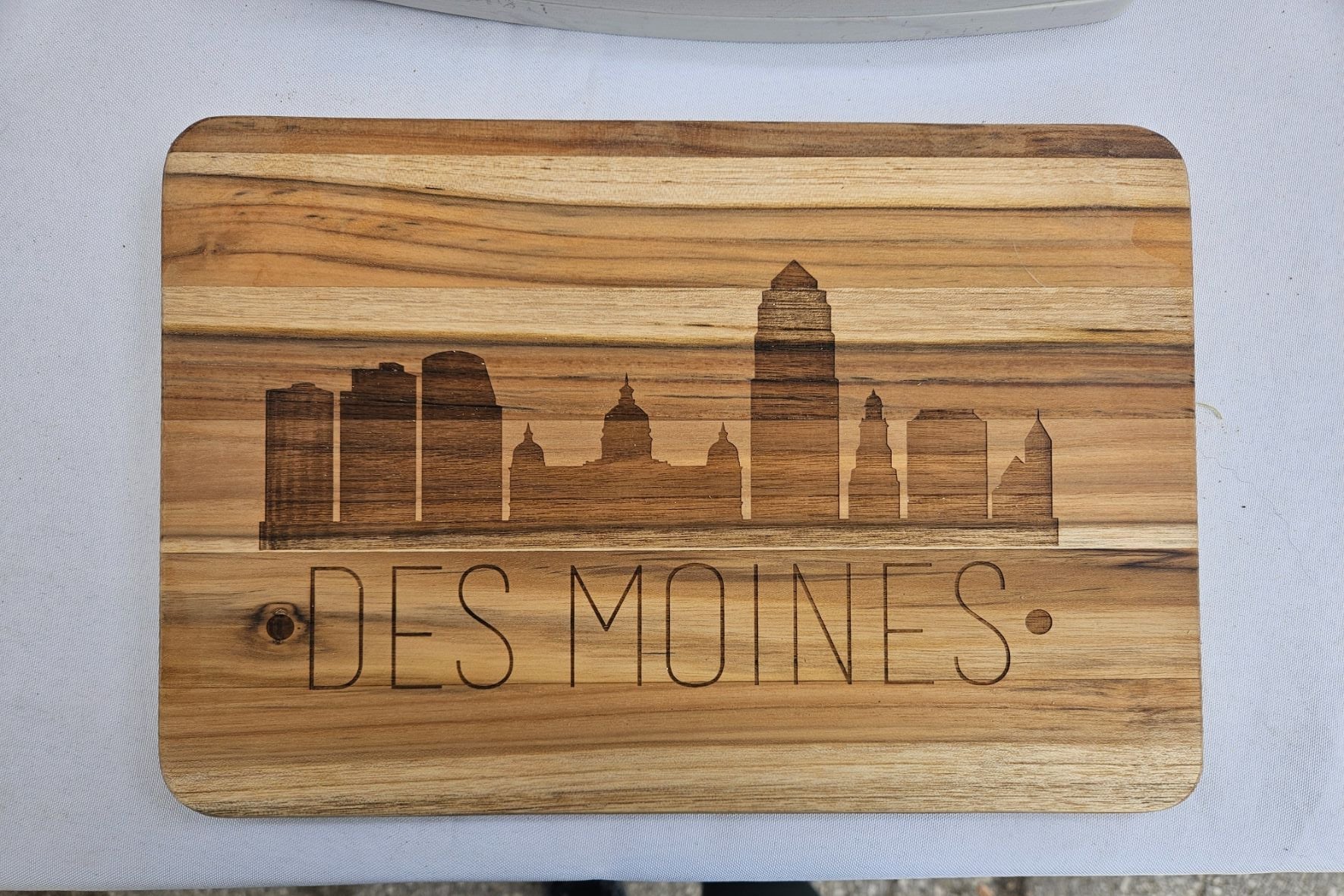 Wooden cutting board with engraved 'Des Moines' and skyline design on a white surface.
