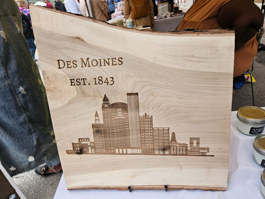 Wooden plaque with 'Des Moines, EST. 1843' and city skyline engraving on a table.