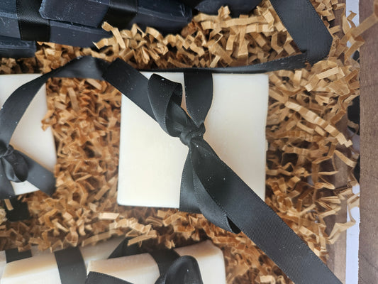 White candles with black ribbons in a decorative box with brown paper