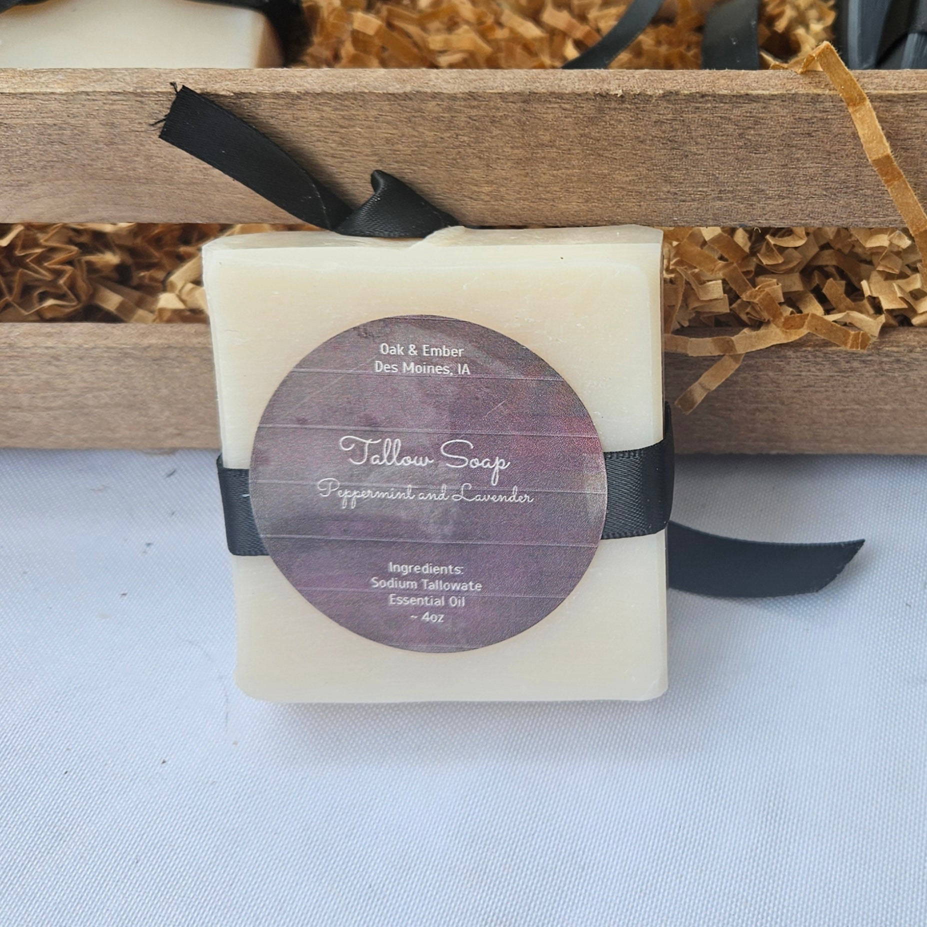 Bar soaps with black ribbons and labels in a wooden crate on a white surface.